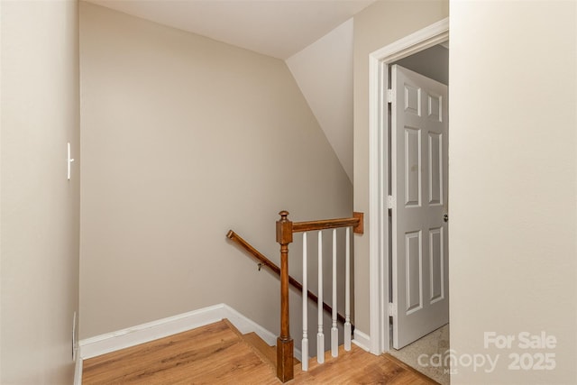 staircase featuring baseboards, wood finished floors, and vaulted ceiling