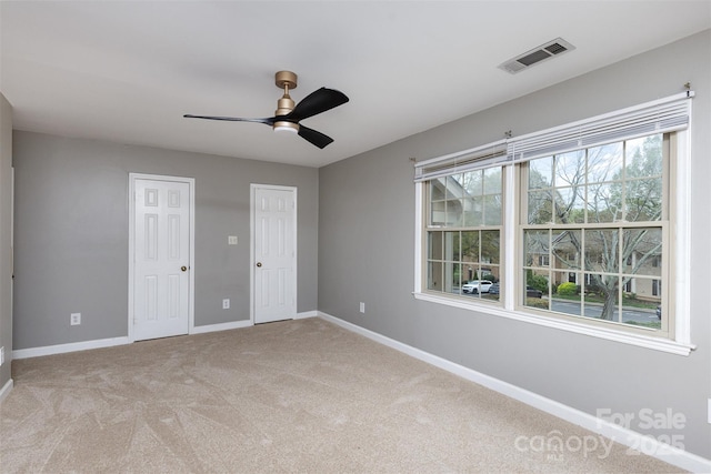 unfurnished bedroom with light colored carpet, multiple closets, baseboards, visible vents, and ceiling fan