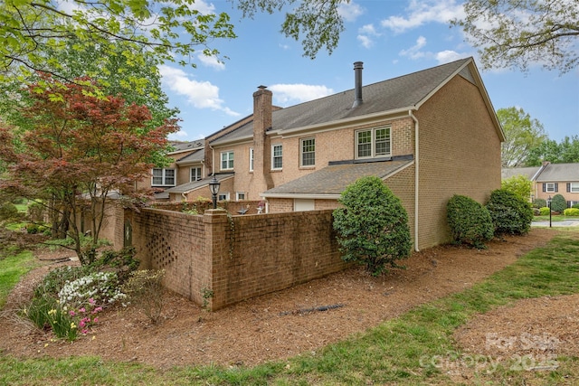 rear view of house featuring a chimney, fence, and brick siding