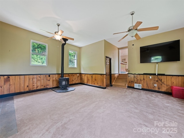 234 Bird Creek Dr, Waynesville, NC 28786 - unfurnished living room with a wood stove, wainscoting, a ceiling fan, carpet, and wood walls