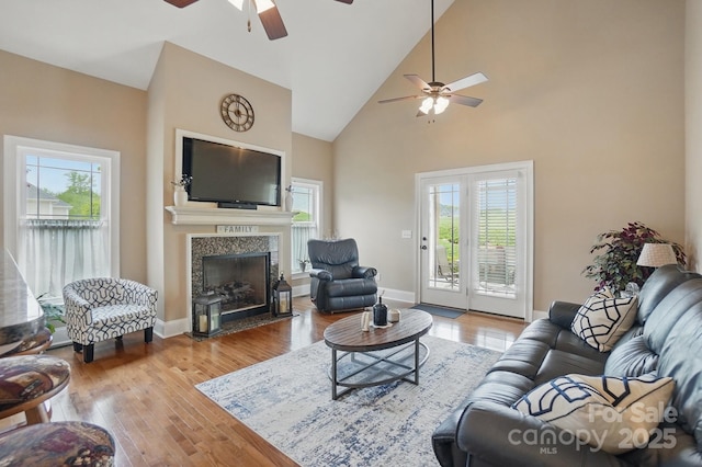living area featuring high vaulted ceiling, a ceiling fan, a fireplace, wood-type flooring, and baseboards