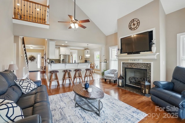 living room with high vaulted ceiling, a ceiling fan, wood finished floors, and a tiled fireplace