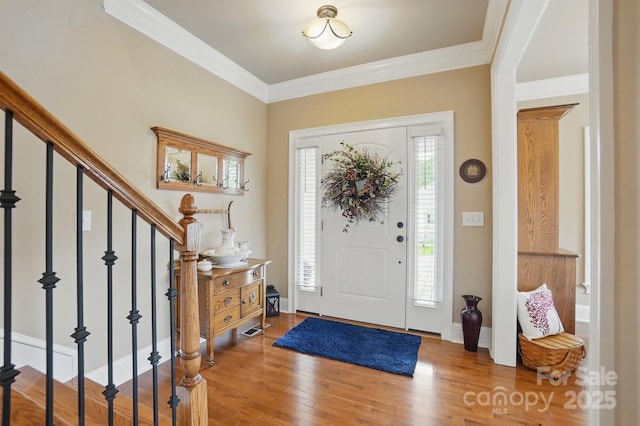 foyer entrance with stairway, baseboards, ornamental molding, and wood finished floors