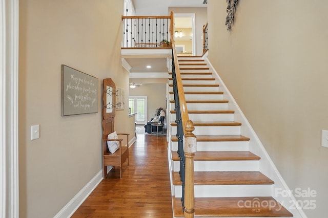 stairway featuring wood finished floors, a high ceiling, and baseboards