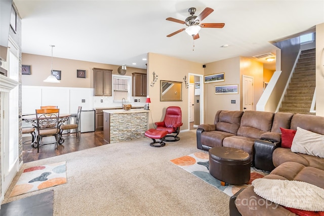 living room with dark carpet, a ceiling fan, visible vents, and stairs