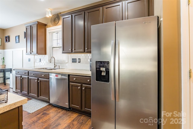 kitchen featuring a sink, dark brown cabinets, stainless steel appliances, dark wood-type flooring, and backsplash