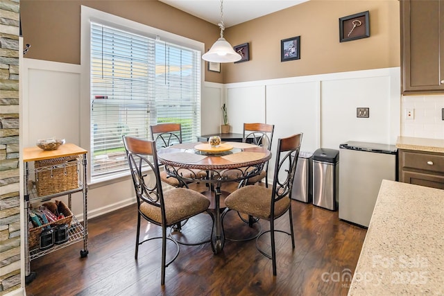dining area with a wealth of natural light, a decorative wall, a wainscoted wall, and dark wood finished floors
