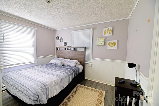 bedroom featuring crown molding, wainscoting, baseboard heating, a textured ceiling, and wood finished floors