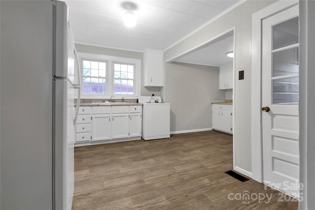 kitchen with crown molding, washer / dryer, freestanding refrigerator, white cabinets, and wood finished floors