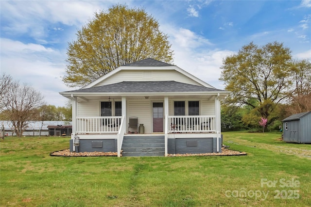 bungalow-style home with an outbuilding, a front yard, covered porch, and roof with shingles
