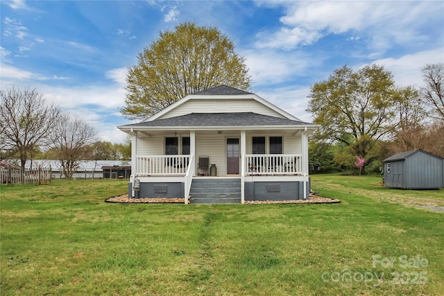 view of front facade featuring a front yard, covered porch, an outbuilding, a storage shed, and a shingled roof
