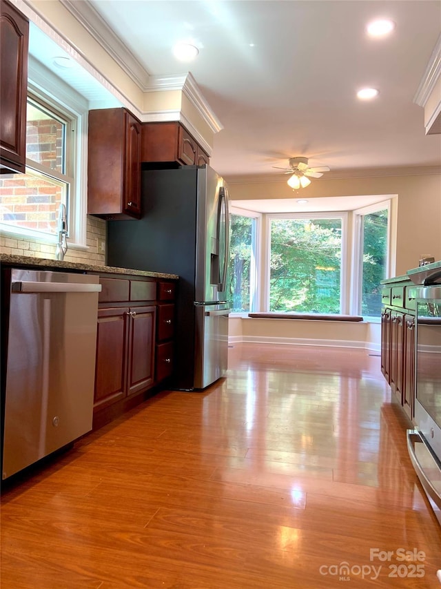 kitchen featuring crown molding, dark stone countertops, ceiling fan, stainless steel appliances, and light wood finished floors