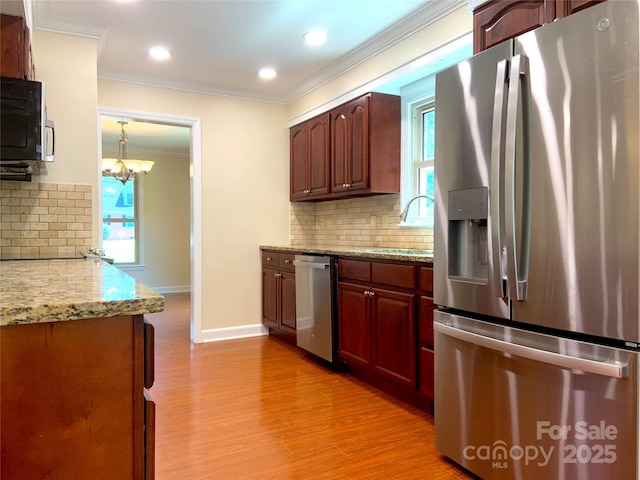 kitchen with light wood finished floors, stainless steel appliances, a sink, decorative backsplash, and crown molding