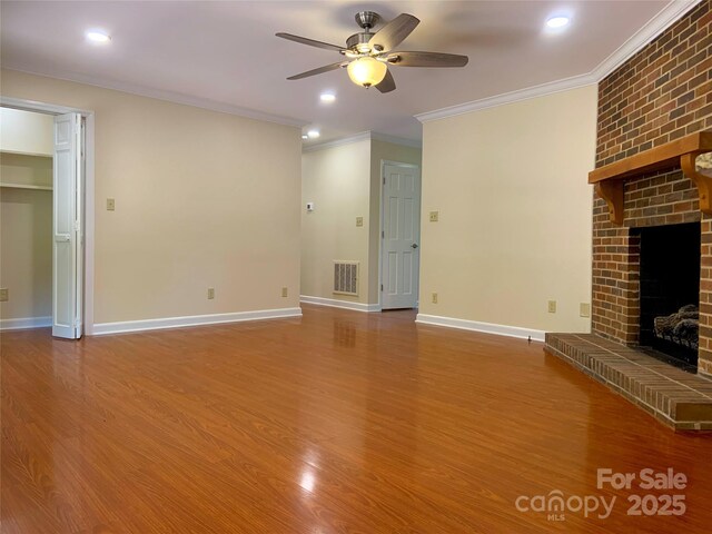 unfurnished living room featuring wood finished floors, visible vents, crown molding, a fireplace, and ceiling fan