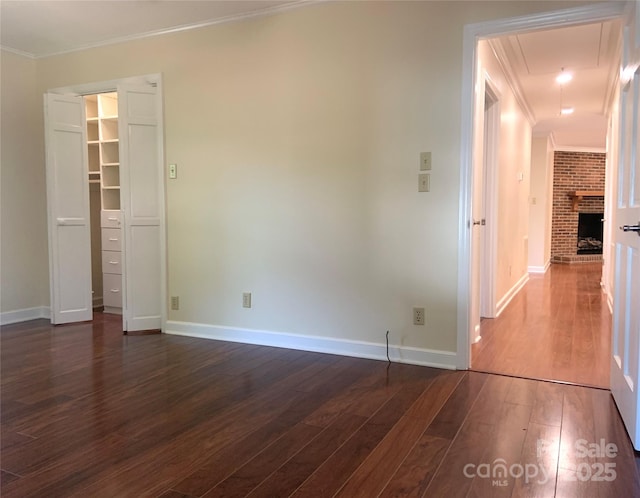 unfurnished bedroom with attic access, baseboards, a spacious closet, crown molding, and dark wood-type flooring