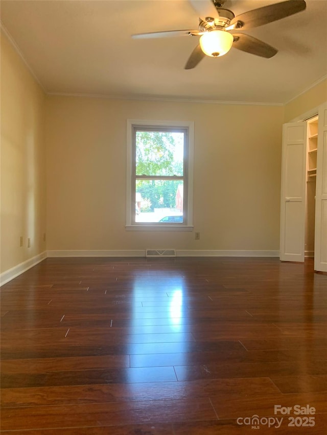 unfurnished room featuring dark wood finished floors, baseboards, visible vents, a ceiling fan, and ornamental molding