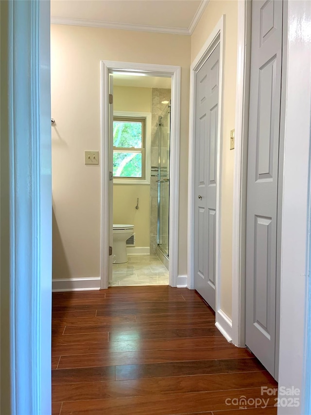 hall featuring baseboards, wood finished floors, and crown molding