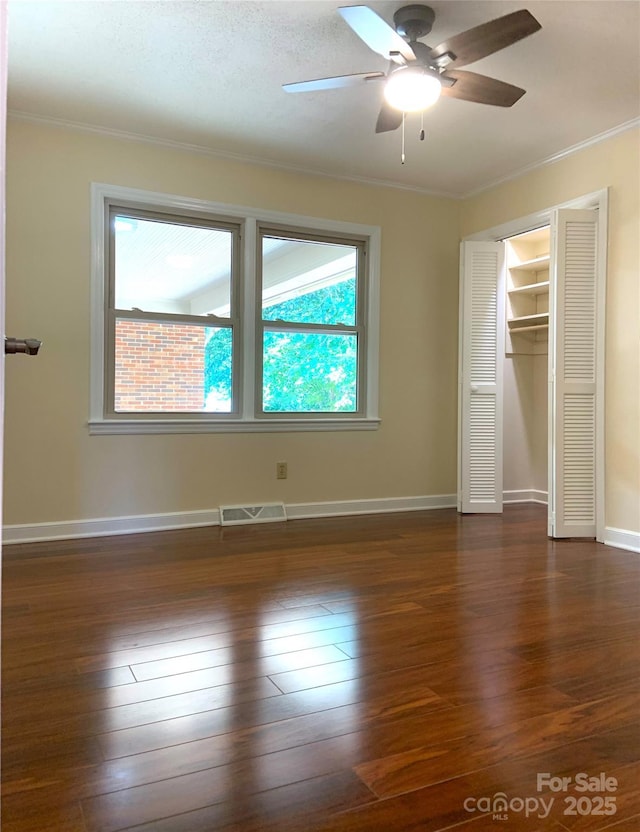 unfurnished bedroom with dark wood-style floors, crown molding, a closet, ceiling fan, and visible vents