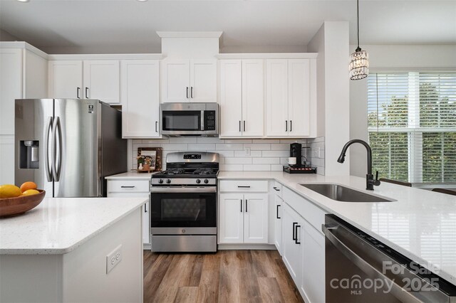 kitchen featuring appliances with stainless steel finishes, a sink, decorative backsplash, wood finished floors, and white cabinets