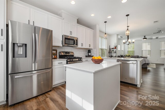 kitchen with appliances with stainless steel finishes, a peninsula, open floor plan, a kitchen island, and dark wood finished floors