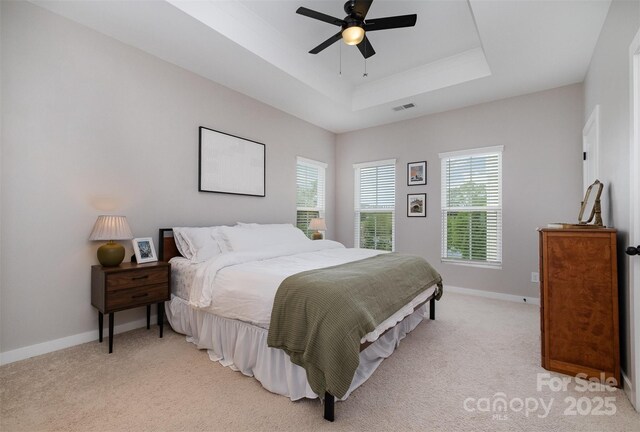 bedroom with a tray ceiling, light colored carpet, and baseboards