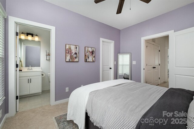 bedroom with light carpet, a ceiling fan, ensuite bathroom, baseboards, and a sink