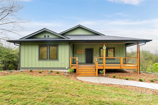 view of front facade featuring a shingled roof, board and batten siding, a front lawn, and covered porch