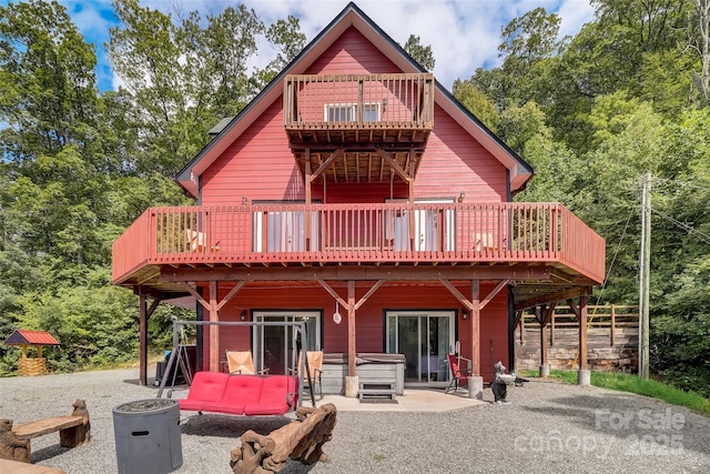rear view of property featuring a forest view, a patio area, a deck, and a hot tub