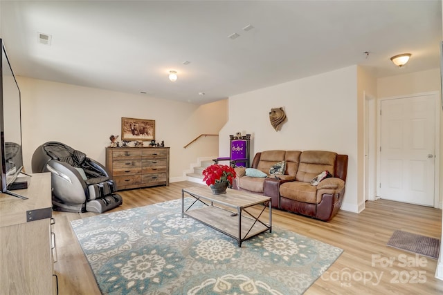 living room with visible vents, baseboards, light wood finished floors, and stairs