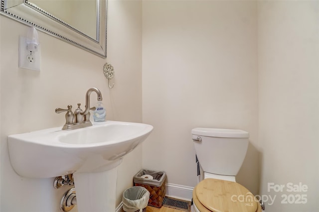 half bathroom with visible vents, baseboards, a sink, and toilet
