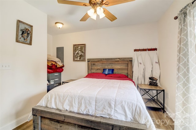 bedroom with wood finished floors, baseboards, a ceiling fan, and electric panel
