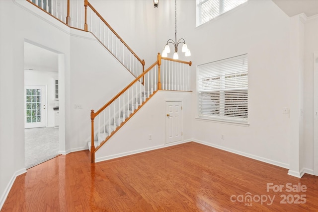 interior space with baseboards, a notable chandelier, a high ceiling, wood finished floors, and stairs