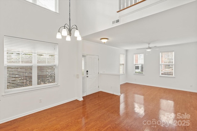 empty room with ceiling fan with notable chandelier, visible vents, a high ceiling, wood finished floors, and baseboards