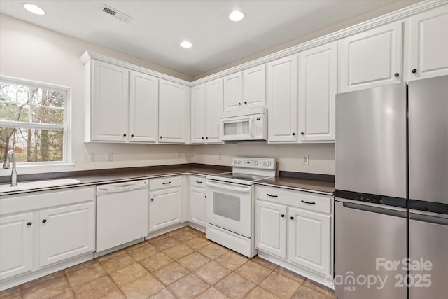 kitchen with white appliances, visible vents, white cabinets, a sink, and dark countertops