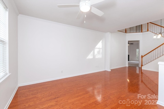 unfurnished living room featuring baseboards, ornamental molding, a ceiling fan, stairs, and wood finished floors