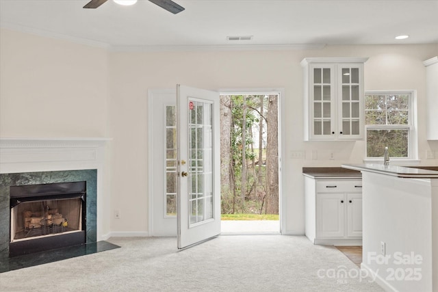 interior space with crown molding, ceiling fan, light colored carpet, visible vents, and a premium fireplace