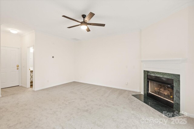 unfurnished living room featuring baseboards, ornamental molding, ceiling fan, carpet, and a premium fireplace