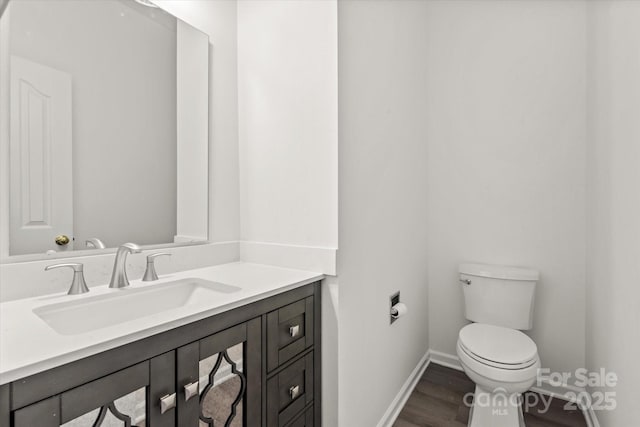 half bathroom featuring vanity, baseboards, toilet, and wood finished floors