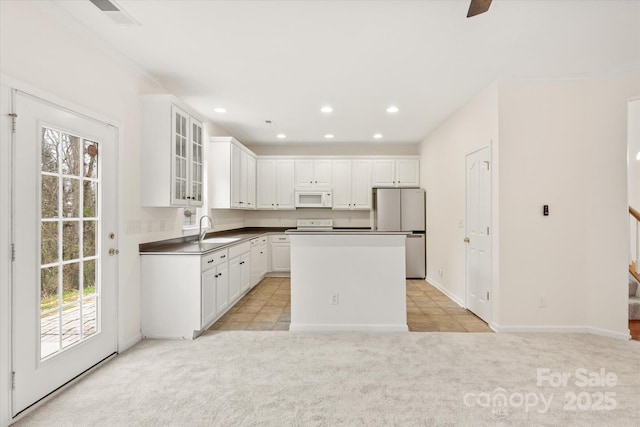 kitchen featuring a sink, white microwave, light colored carpet, and freestanding refrigerator