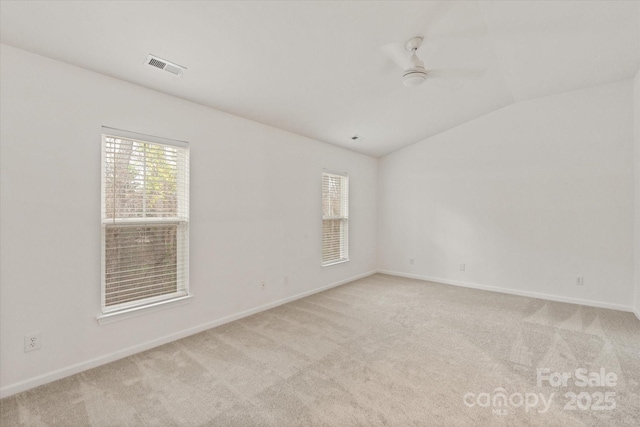 empty room with visible vents, baseboards, ceiling fan, vaulted ceiling, and light colored carpet