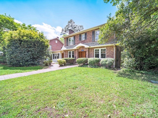 view of front of house with brick siding, a front lawn, and a chimney