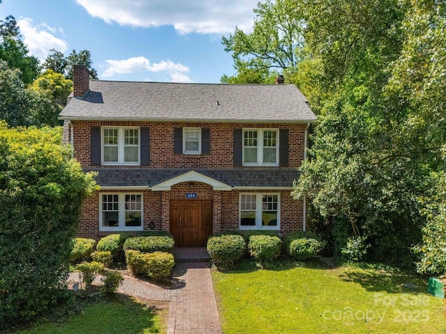 view of front of property with a chimney, a shingled roof, a front lawn, and brick siding