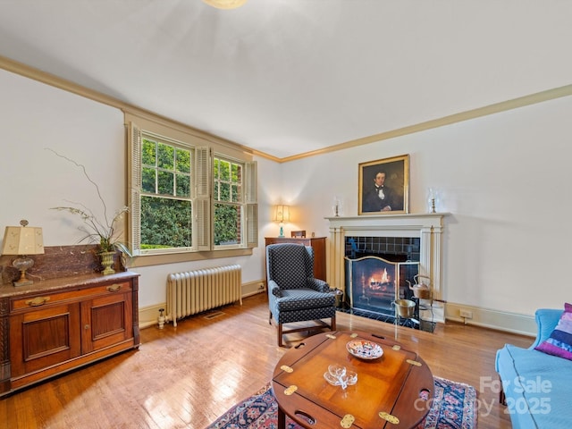 living room with ornamental molding, light wood finished floors, radiator, and a fireplace