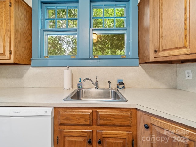 kitchen with white dishwasher, light countertops, and a sink