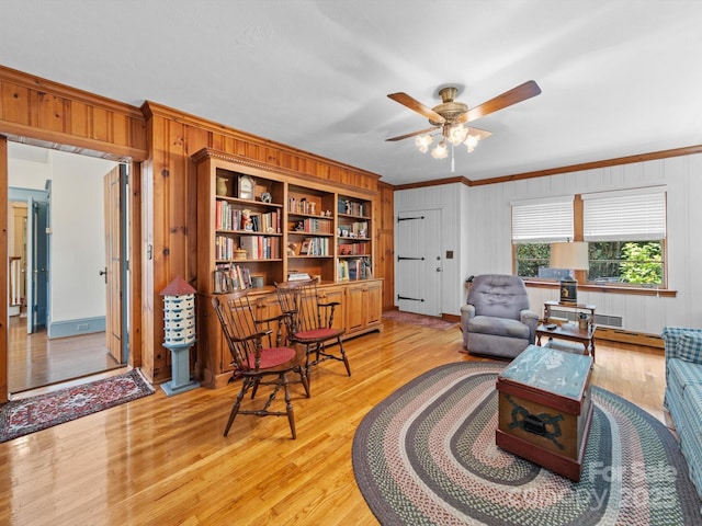 sitting room featuring wooden walls, light wood-style floors, ornamental molding, and ceiling fan