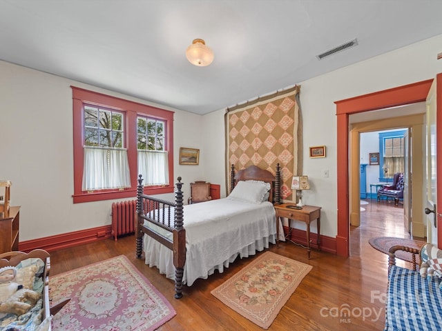 bedroom featuring radiator heating unit, visible vents, baseboards, and wood finished floors