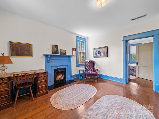 sitting room with a fireplace with flush hearth, visible vents, baseboards, and wood finished floors