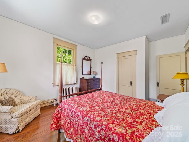 bedroom with baseboard heating, wood finished floors, radiator heating unit, and visible vents