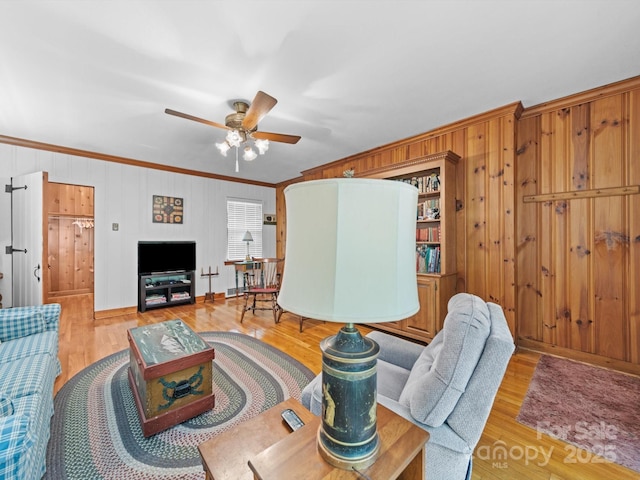 living area featuring light wood finished floors, a ceiling fan, and crown molding