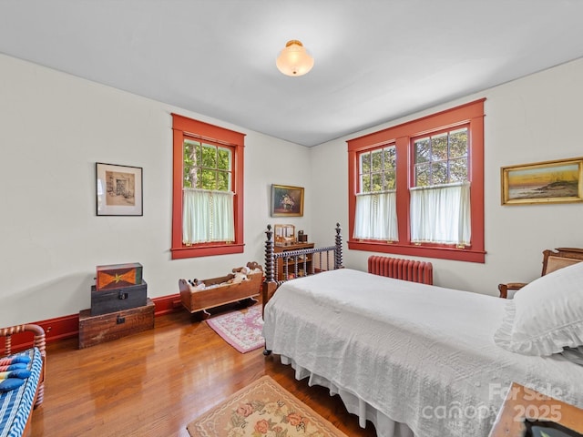 bedroom with radiator heating unit, multiple windows, baseboards, and wood finished floors
